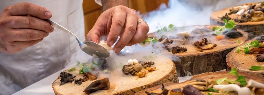 Kokk legger opp mat på tallerkener lagd av trestammer. Foto.