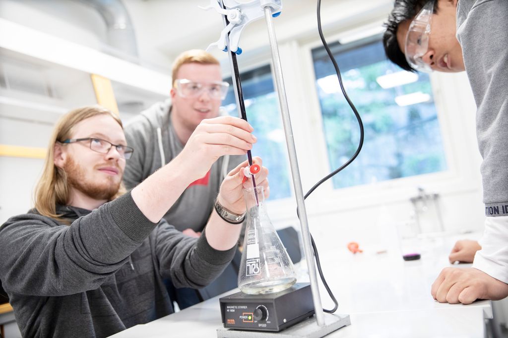 En person tapper væske fra et tynt rør til kolbe på et måleapparat. Foto.