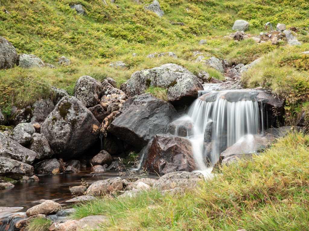 Fjellandskap med ein liten foss som renn ut i ein bekk. Foto.