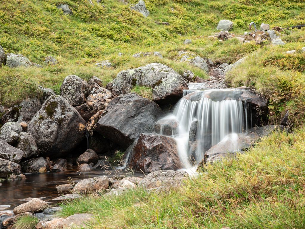 Fjellandskap med en liten foss som renner ut i en bekk. Foto.