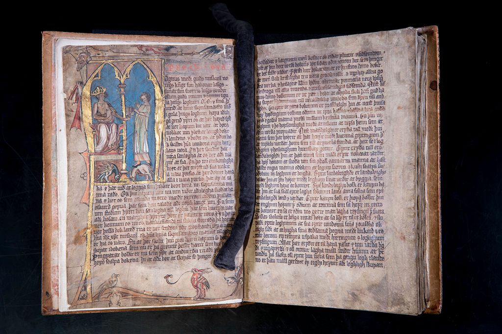 En dobbeltside med forgylt illustrasjon på den ene siden. Skriften er gotisk. Foto. 