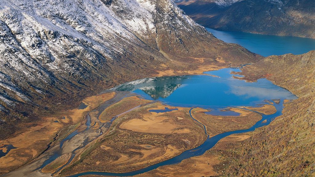 Lausmassar avsette i ein liten innsjø i eit fjellandskap. Haustleg bilete med nysnø i fjella. Foto.