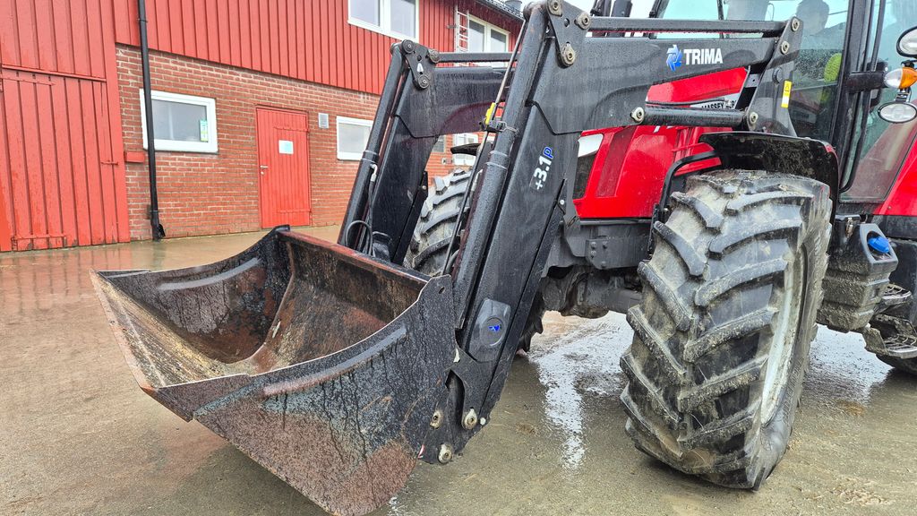 Fronten på ein traktor med ei lasteskuffe montert på frontlastararmane. Foto.