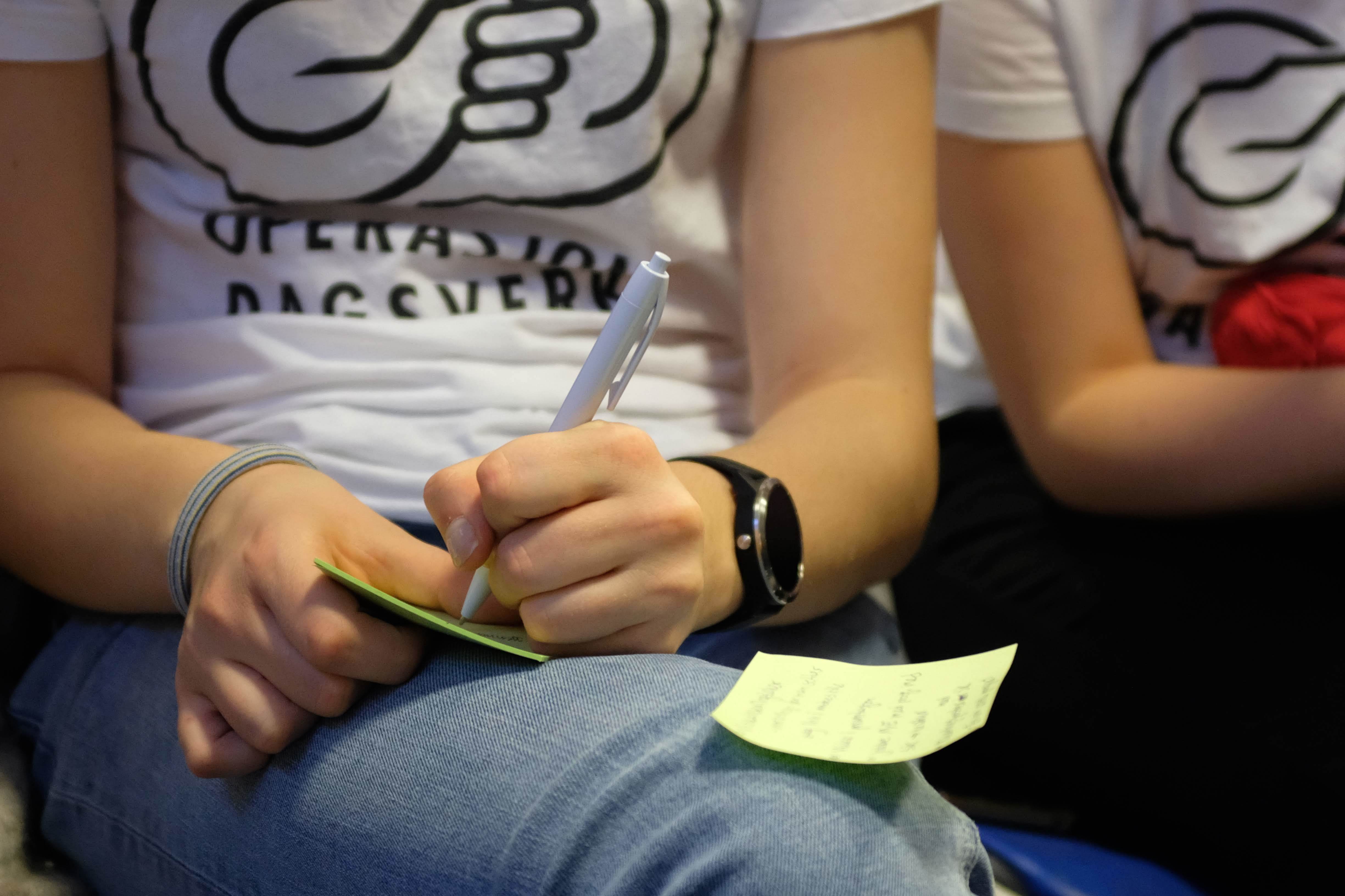 Elev med t-skjorte med logoen til Operasjon Dagsverk noterer på lapp. Foto.