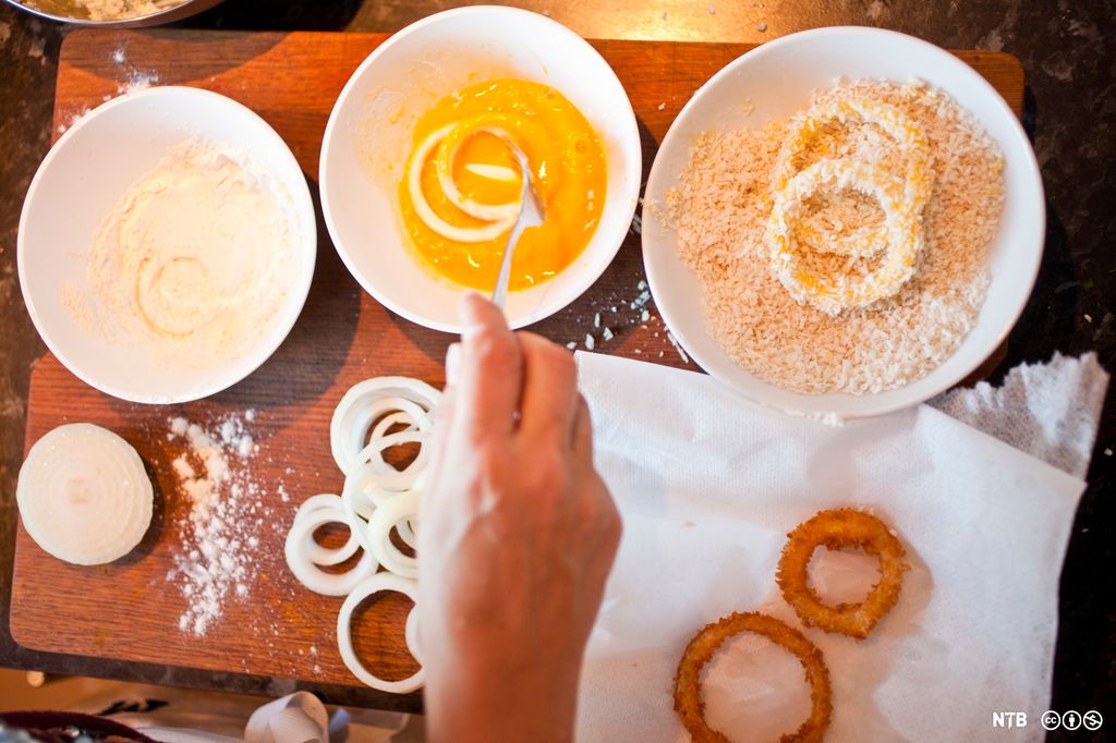 En paneringsstasjon som består av en skål med hvetemel, en skål med egg og en skål med griljermel. I skålen med egg dyppes det løkringer ved hjelp av en gaffel. Foto.