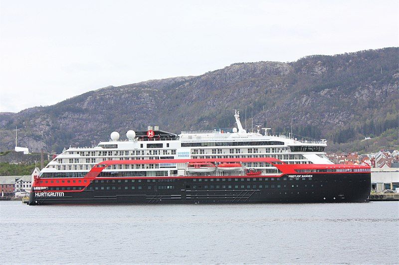 Hurtigruteskipet Fridtjof Nansen ligger til kai. Fjell i bakgrunnen. Foto.