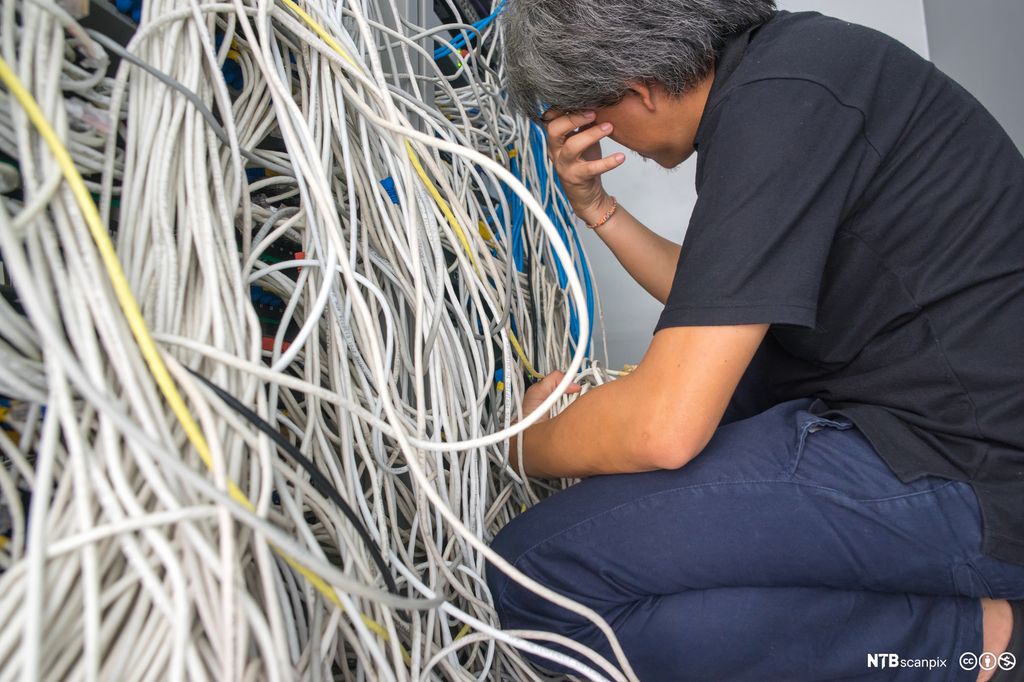 Fortvilet IT arbeider sitter foran et rotete nettverksskap. Foto.