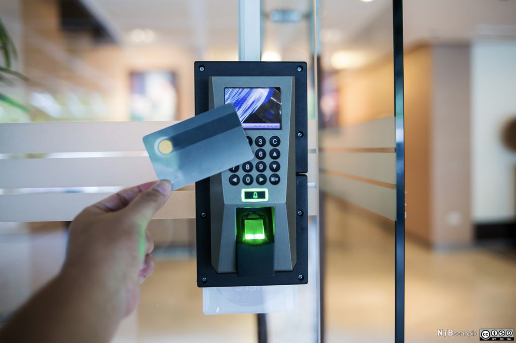 En person holder et kort opp mot en kortleser med tastatur. Foto.