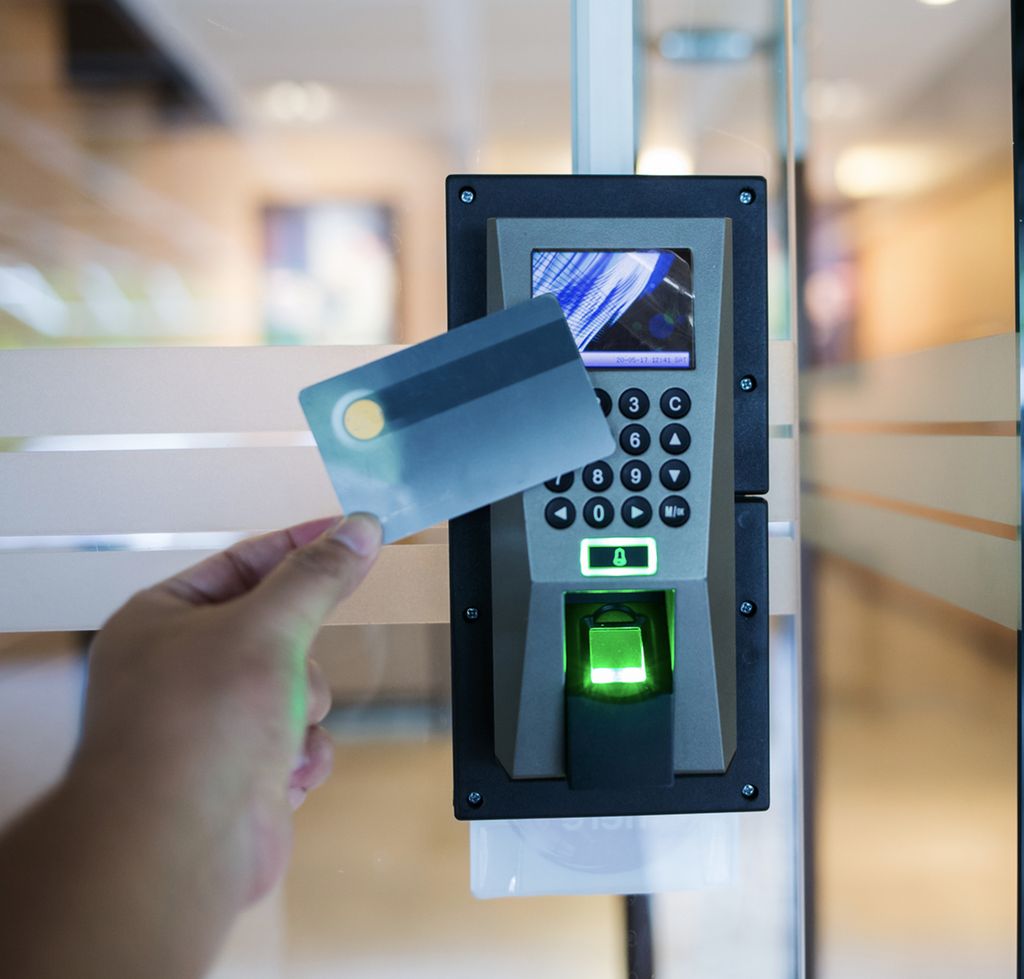 En liten digital enhet for adgangskontroll ved ei dør. Enheten har tastatur, felt for avlesing av adgangskort og en fingeravtrykkleser. Ei hånd holder et kort opp mot feltet for avlesing av adgangskort. Foto.