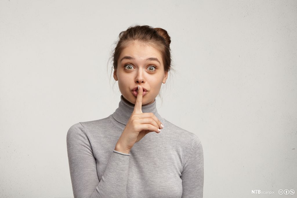Kvinne som viser hysjtegn foran munnen. Foto.