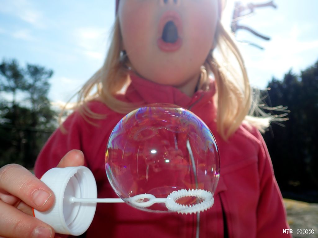 Lita jente blåser såpebobler. Foto.