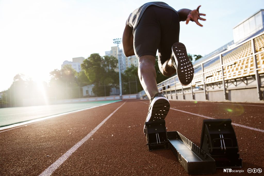 Ung mannlig idrettsutøver sett bakfra på startstreken. Foto.