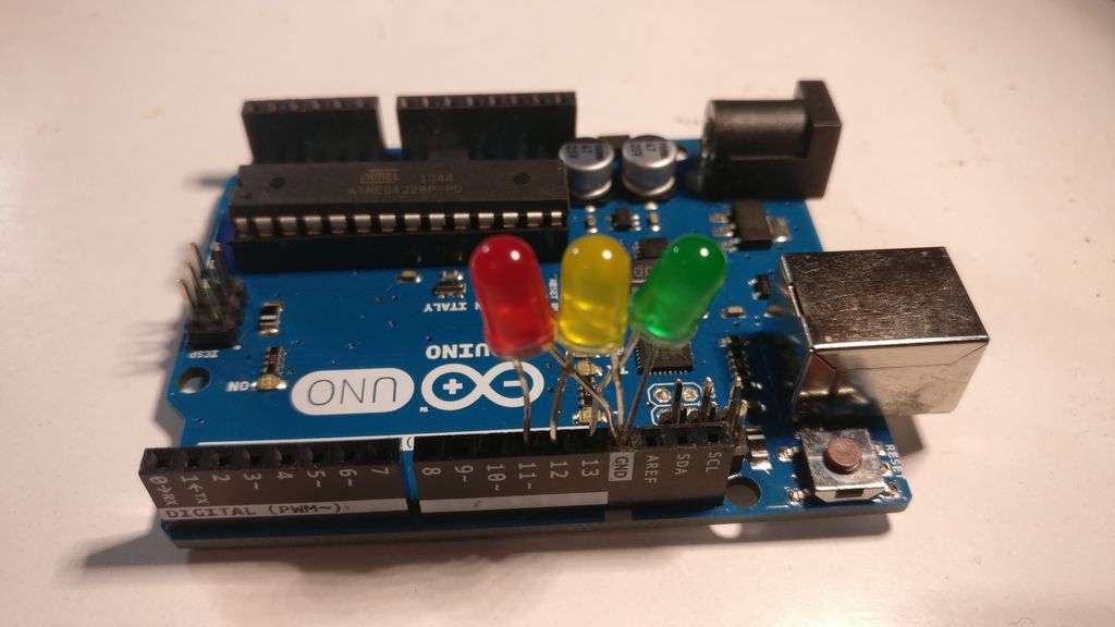 Arduino mikrokontroller med tre lysdioder med fargene rødt, gult og grønt tilkopla pinnene 11, 12, 13 og GND. Foto.