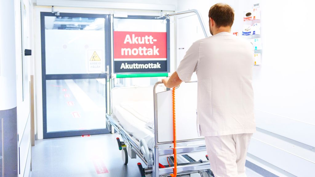 Person i uniform for helsepersonell triller ei tom seng mot ei dør merket akuttmottak. Foto.