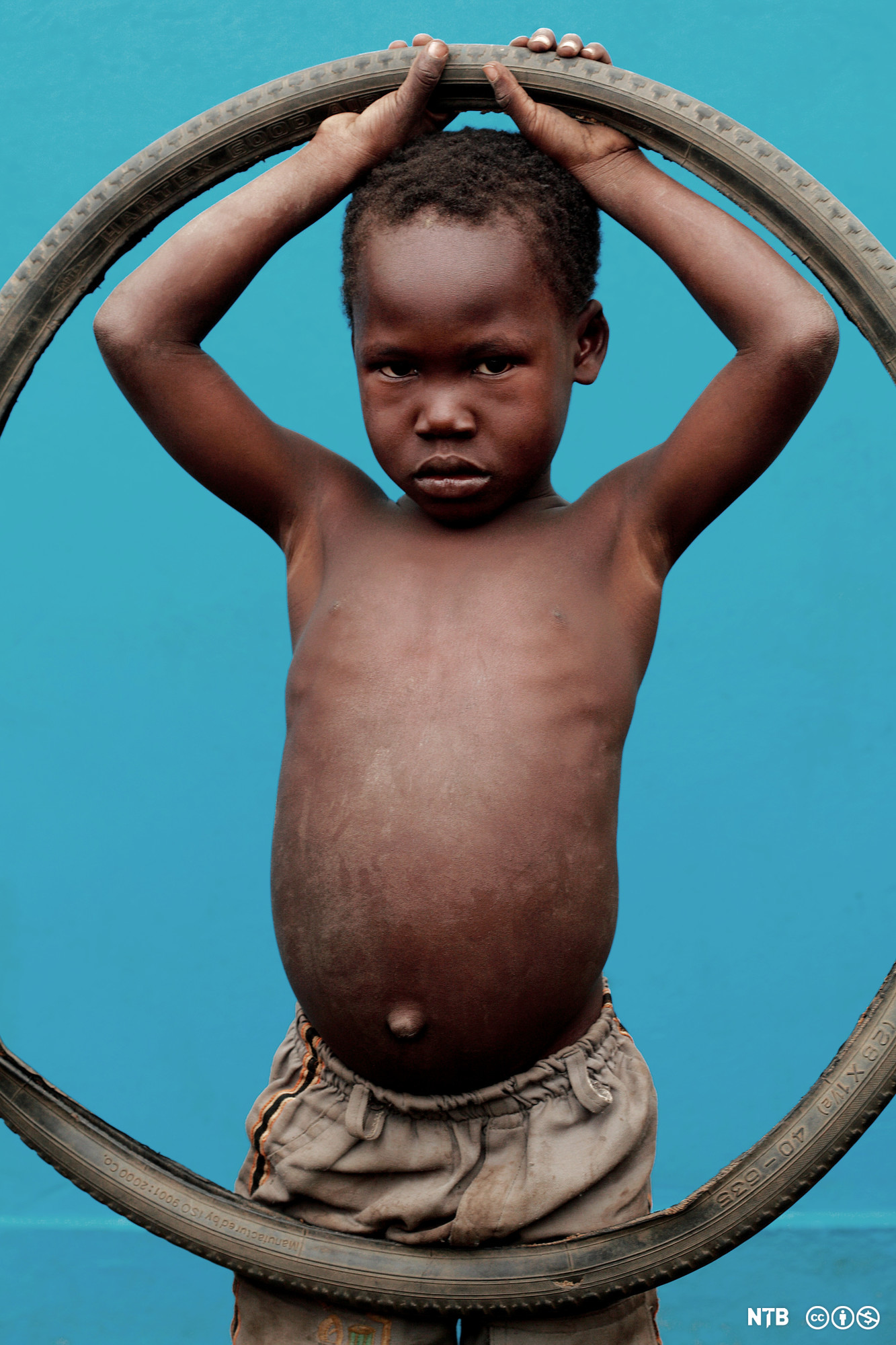 En liten mørkhudet gutt holder opp et sykkeldekk. Foto.