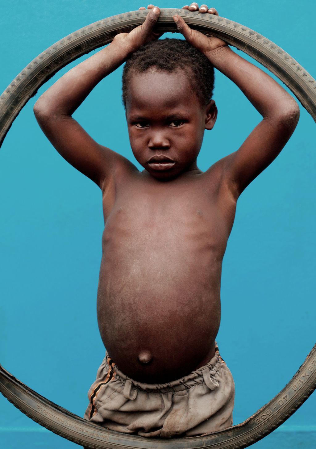 En liten mørkhudet gutt holder opp et sykkeldekk. Foto.