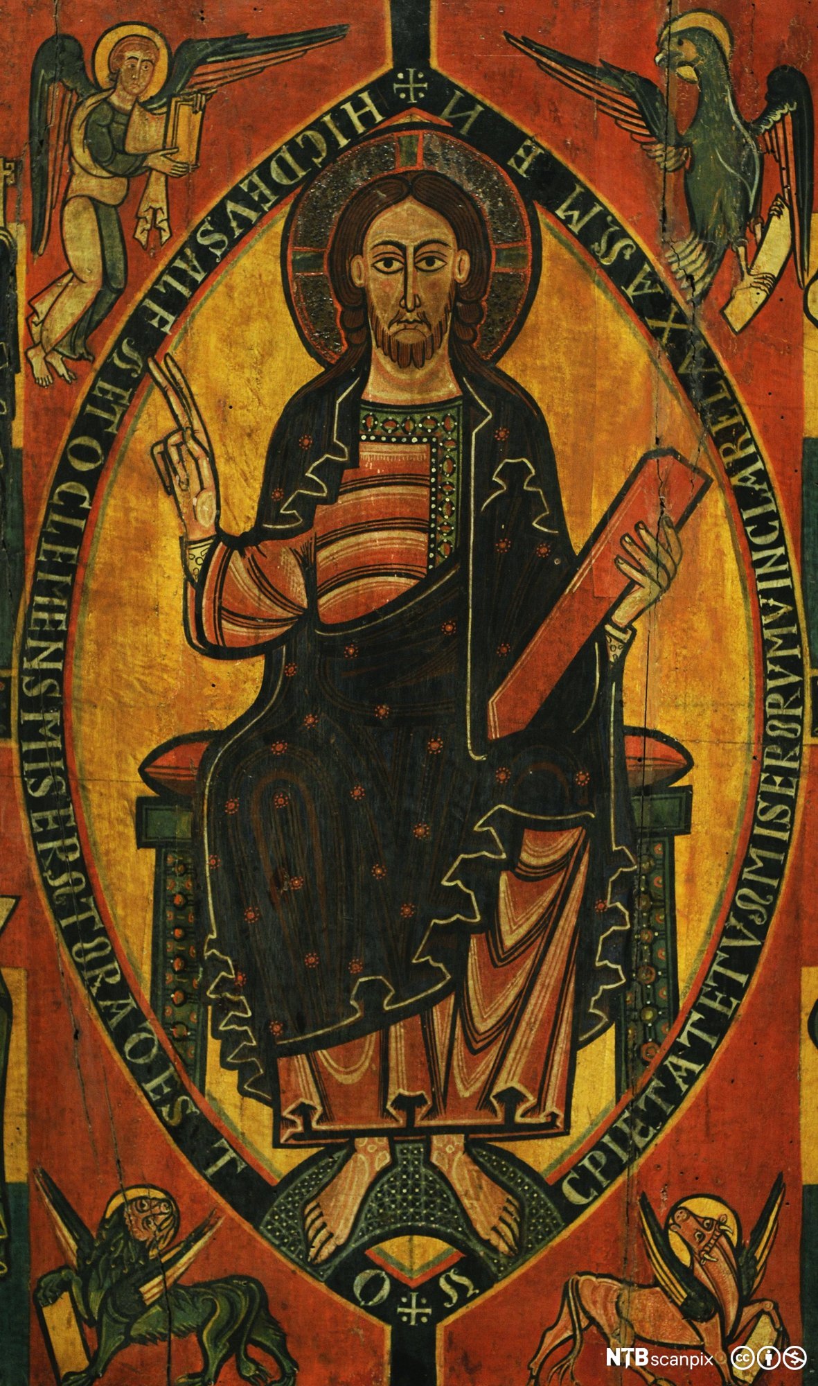 Jesus holder en bok i den ene hånden og holder opp to fingre med den andre. Rundt hodet er en glorie. Han er omgitt av tekst og fire ulike figurer. Maleri.