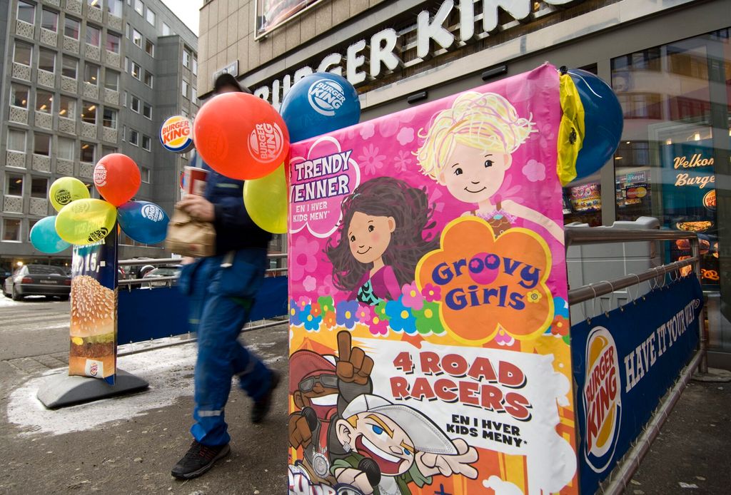 Utenfor en Burger King-restaurant er det plassert en reklameplakat med friske, sterke farger og illustrasjoner av fire forskjellige personer. På plakaten står det "Trendy venner. En i hver kids meny" og "4 road racers. En i hver kids meny". Foto.