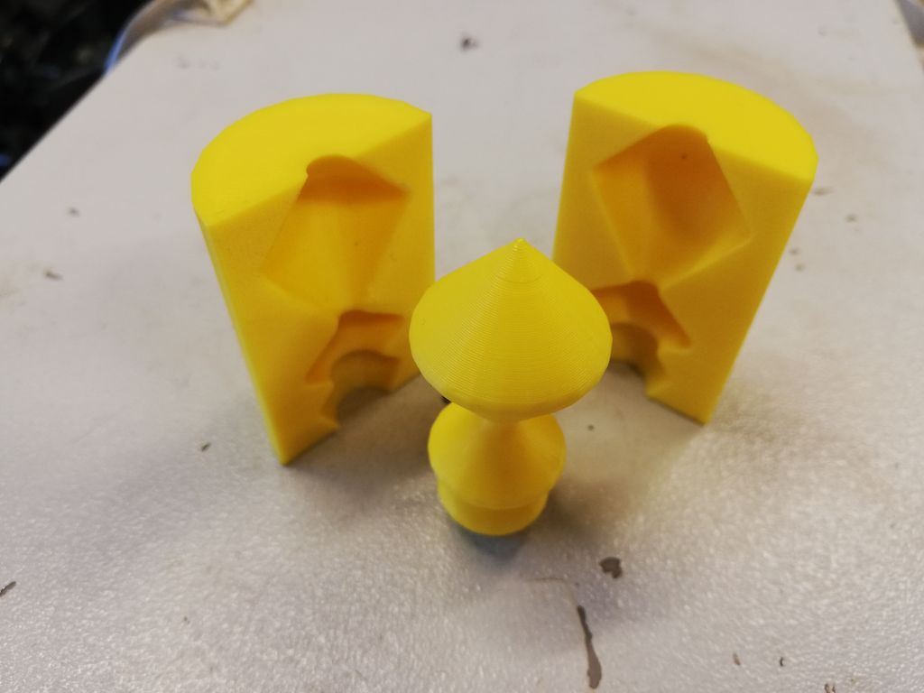 En gul pynteknott og to plastdeler som er utskåret slik at knotten passer inn mellom de to. Foto. 