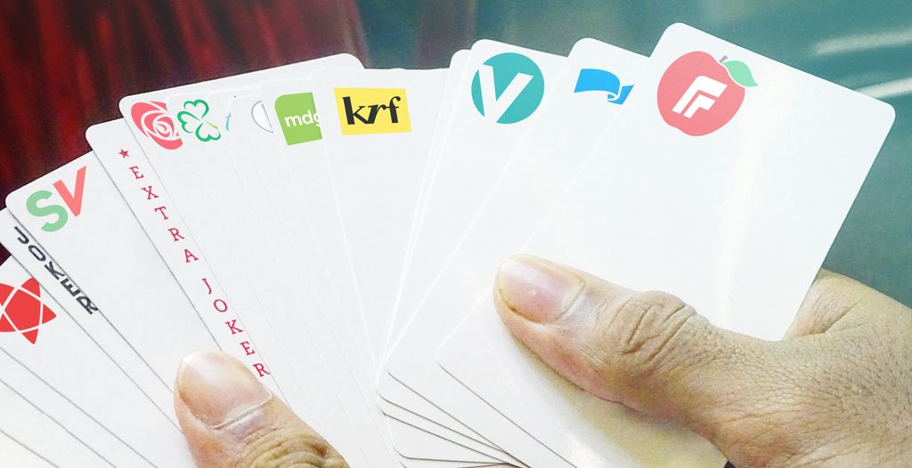 Hånd holder ei vifte med kort med politiske partilogoer på. Foto.