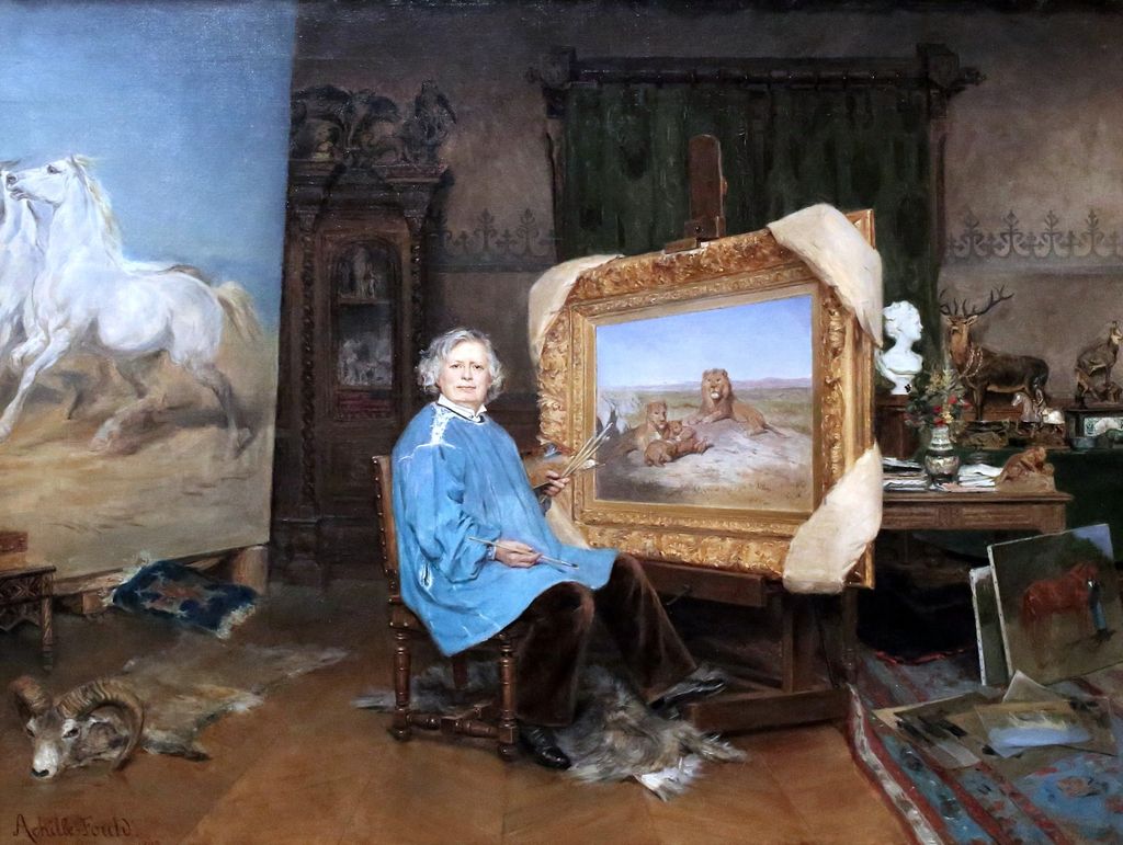 Oljemaleri av en kunstner som maler løver. Bak henne står et stort lerret der motivet er hester. Foto.