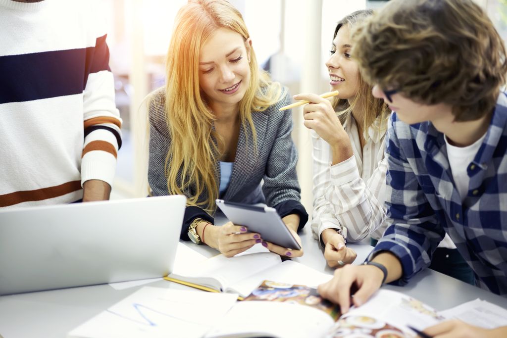 Ei gruppe elever snakker sammen og studerer bøker ved en pult. Foto. 