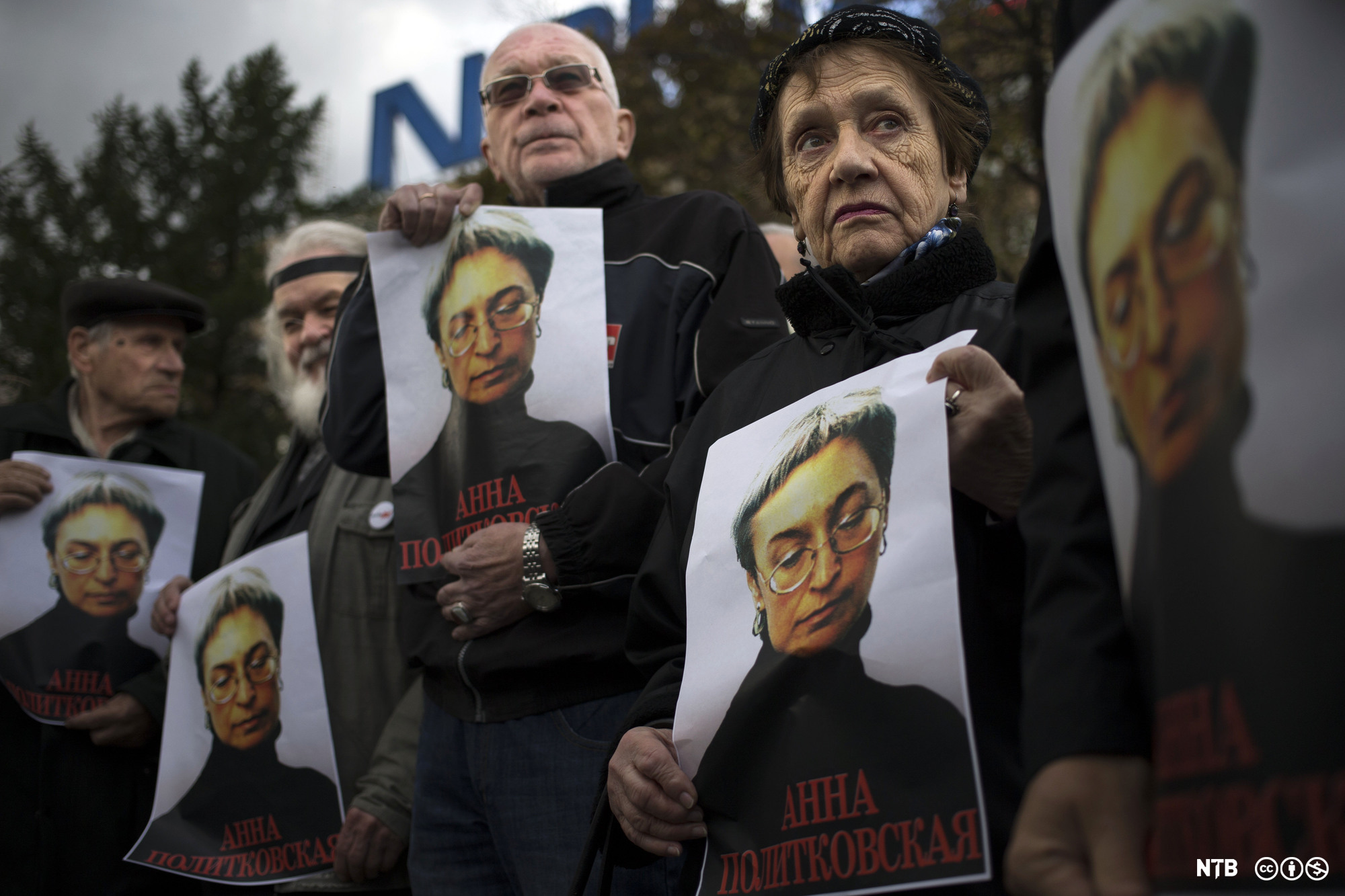 Noen menn og kvinner holder opp hver sin plakat med bilde av en middelaldrende kvinne med briller. Under bildet står navnet til den drepte journalisten Anna Politkovskaja på russisk. Foto.