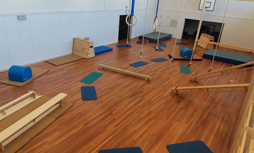 Benker, voltputer, matter, kasser og turnringer i en gymsal. Foto.