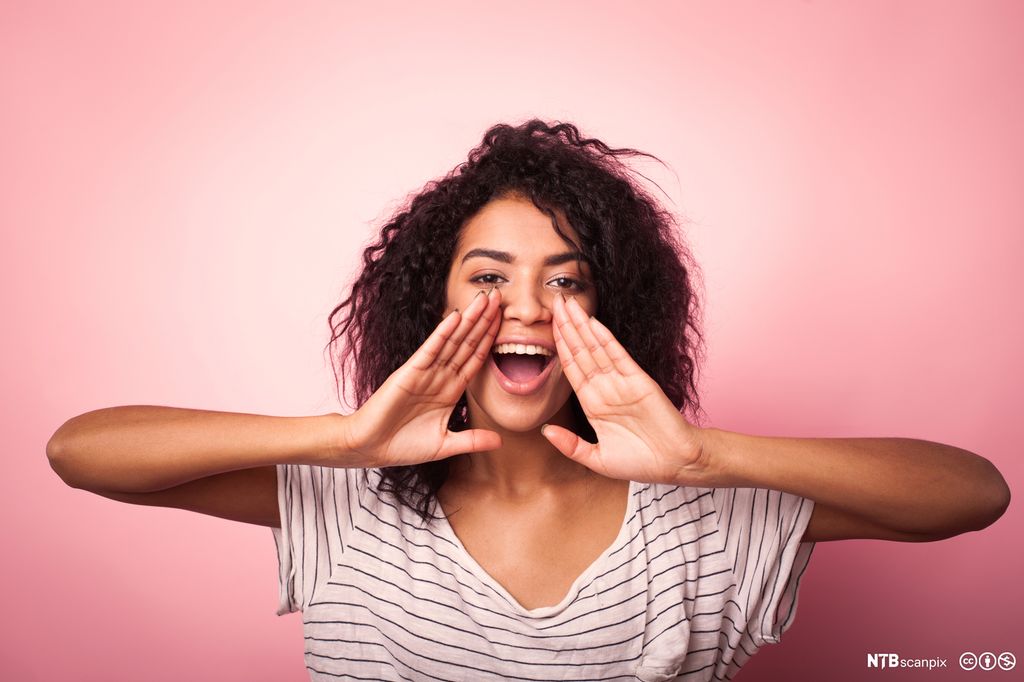 Jente holder hendene opp til munnen og roper. Foto.