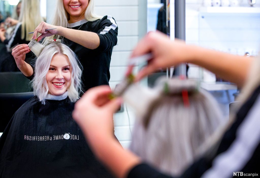 Krølling av hår på en kvinne hos en frisør. Både kunden og frisøren smiler. Foto.