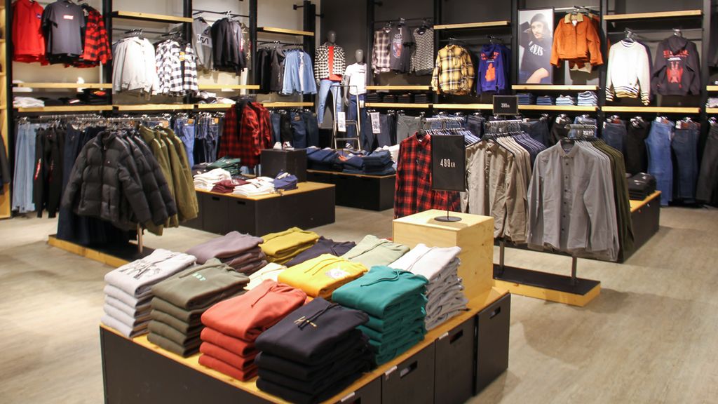 Interiør og klær i en klesbutikk. Det er også plakater rundt omkring i lokalet, og klesstativene har prisplakat. Foto.