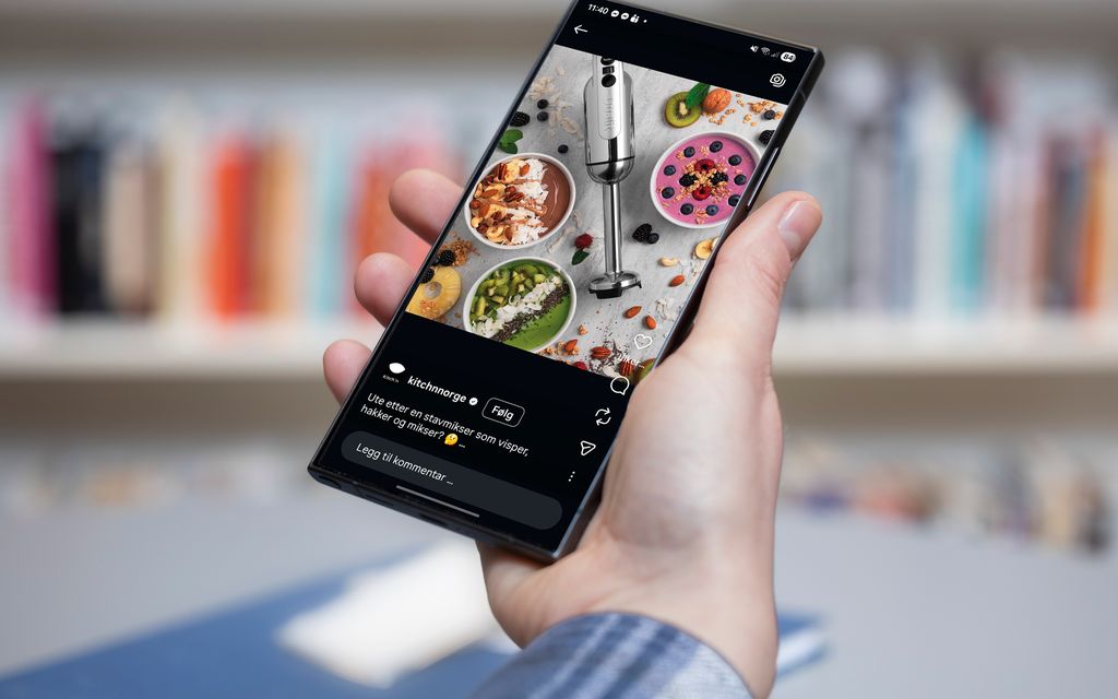 Ei hånd holder en mobiltelefon. På skjermen er det en fargerik reklame for stavmiksere. Foto.