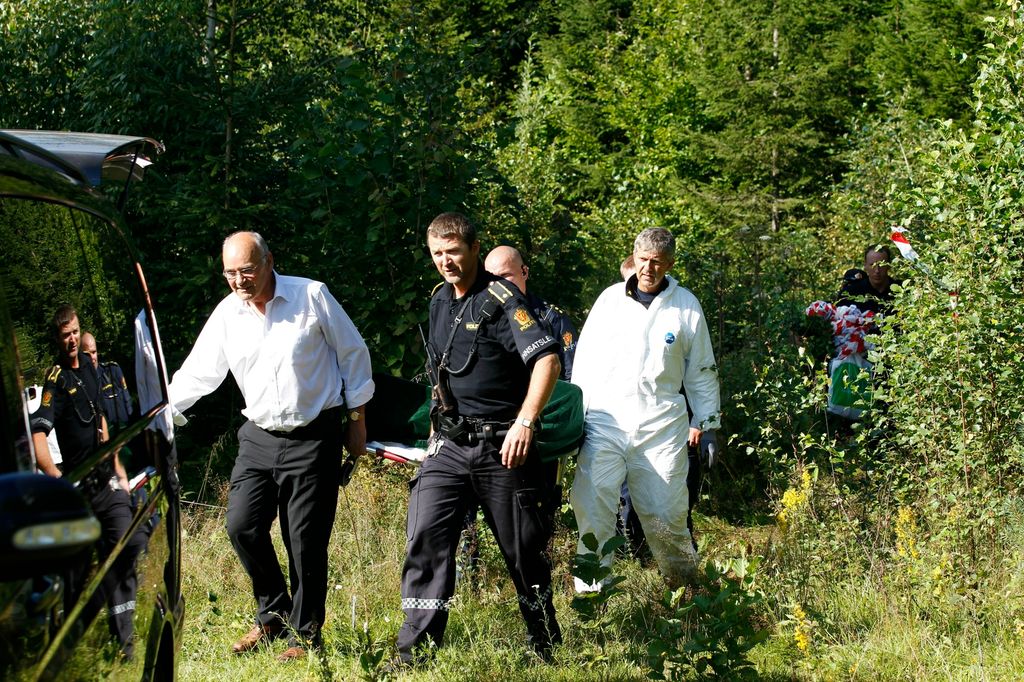 Politifolk i uniform og hvit overtrekksdress bærer bort en omkommet person. Foto.