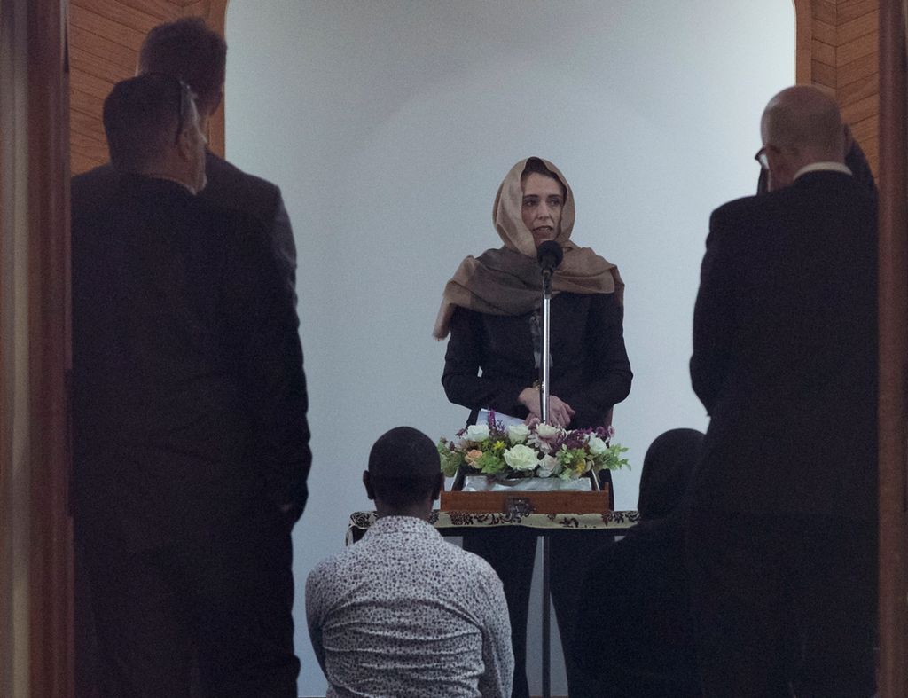 Prime Minister Jacinda Ardern, facing front, talks to members of the Muslim community inside the Al Noor Mosque in Christchurch. She's wearing a traditional headscarf. We only see the backs of her audience.  
