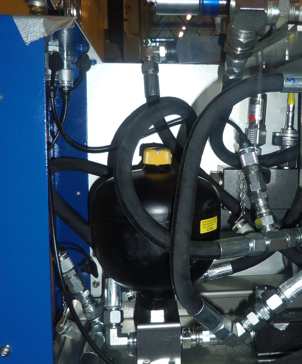 Akkumulator for hydraulisk trykk montert på en hydraulikkenhet med mange slanger og koplinger. Foto.