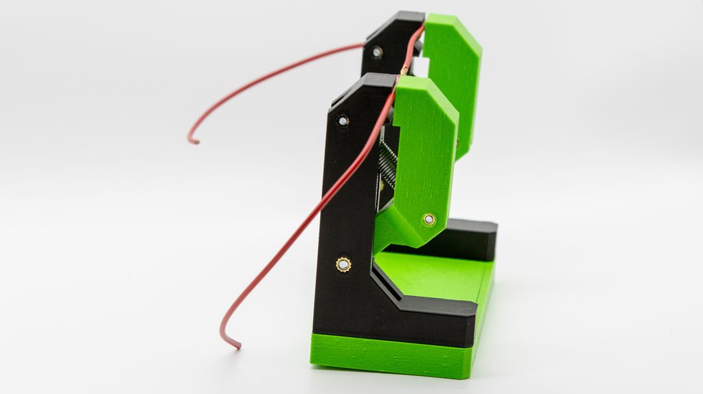 Stativ med to tårn som holder en ledning. Det er ei fjær i tårnet som klemmer ledningen. Foto.