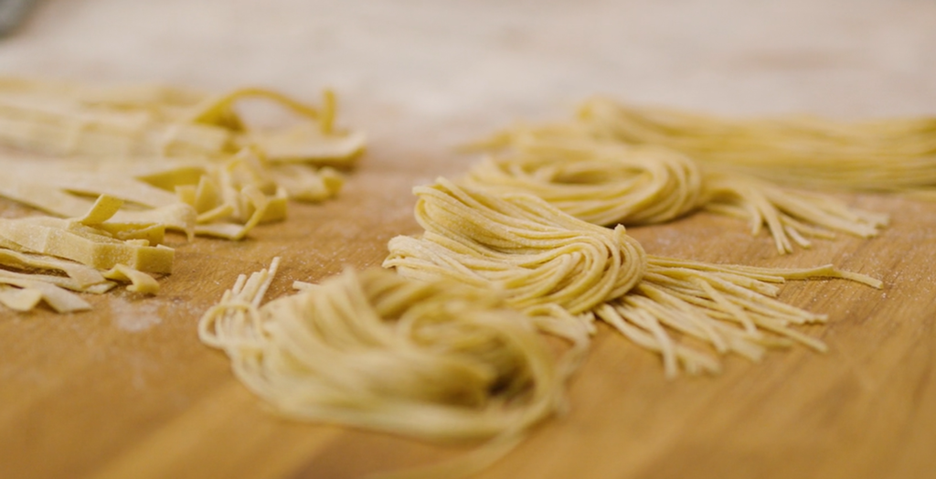 Byggrynspasta som spagetti og tagliatelle liggende på en benk. Foto.