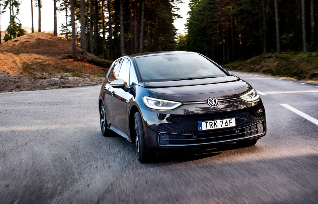 Bil i fart på asfalt. Skog i bakgrunnen. Foto.