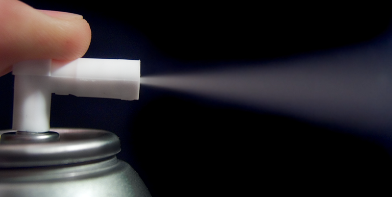 Finger trykker ned ventilen på en sprayboks. Foto.