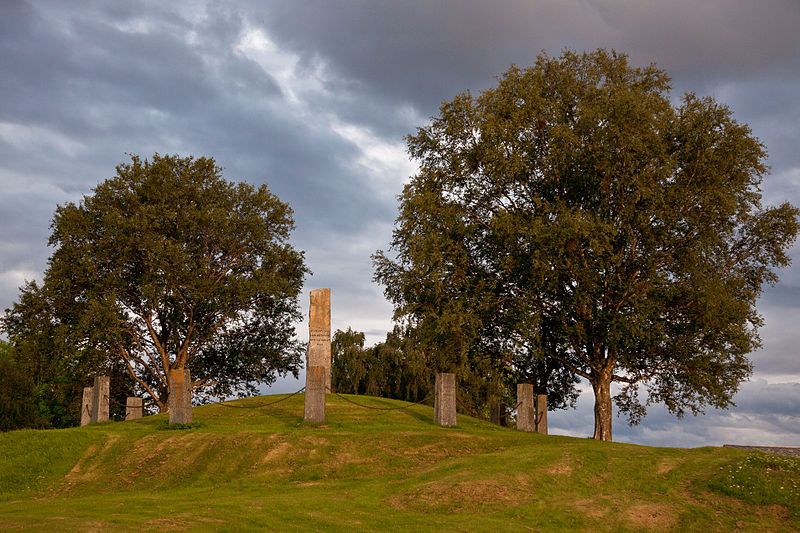 Flere bautasteiner står i ring rundt en hovedbauta på en haug. Foto. 