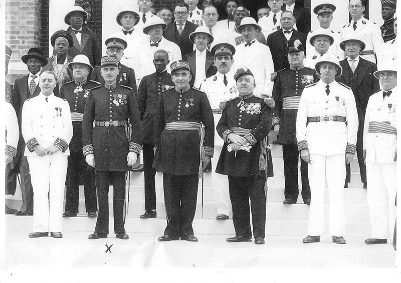 Mange menn står oppstilt i uniformer. Noen har mørke uniformer, andre hvite. Noen har tropehatt. Foto. 