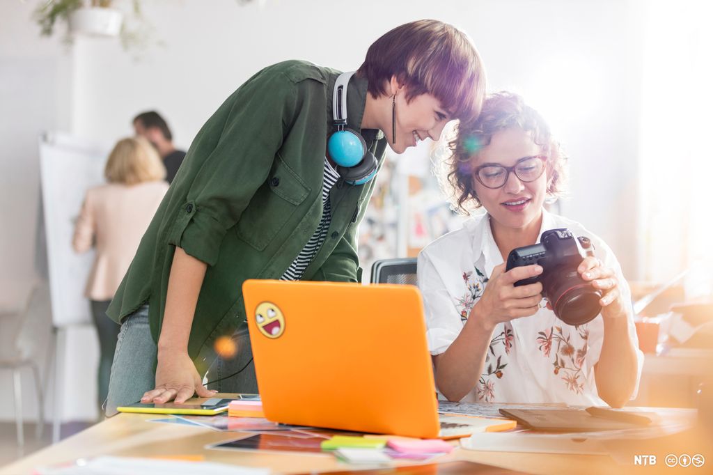 To som ser på ein kameraskjerm ved ein pult. Foto.