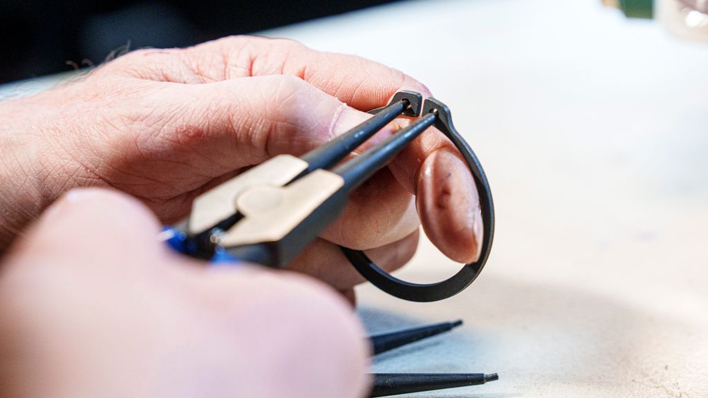 Ei hånd holder ei tang som klemmer mot en ring. Foto.