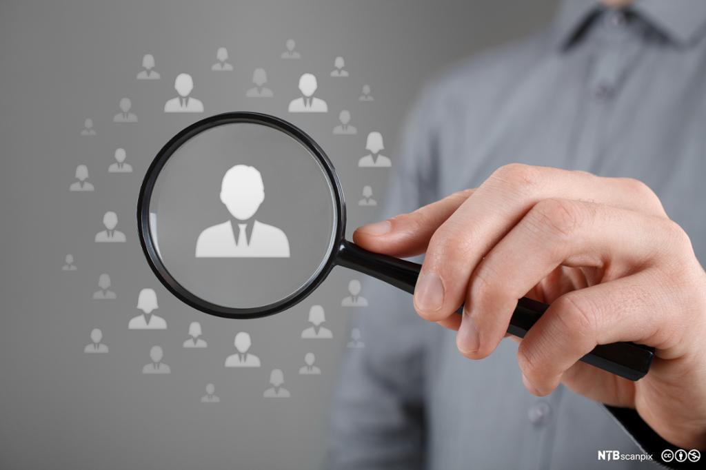 Hånd holder opp et forstørrelsesglass. I glasset er en silhuett av en mann i halvnært utsnitt. Liknende små silhuetter svever rundt glasset. Manipulert foto. 