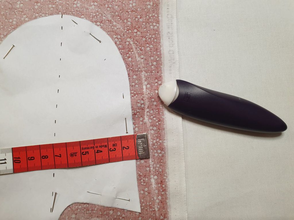 Fotografi av et krittstykke som har markert ei linje som går 1 cm utenfor mønsterkanten. Et målebånd er plassert slik at det viser at avstanden er 1 cm.