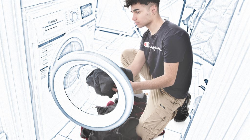 Gutt putter klær inn i vaskemaskinen. Foto.