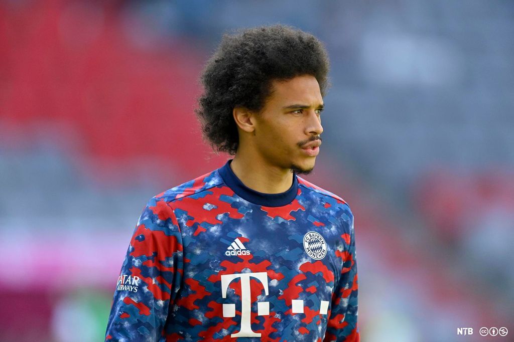Den tyske fotballspilleren Leroy Sané. Han har på seg ei rød og blå Bayern München-klubbdrakt. Han er 25 år, har svartbrunt, sterkt krusete hår, bart og noe skjegg på undersida av haka. Foto.