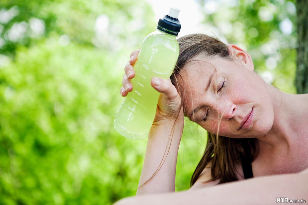 Ung kvinne er sliten og holder drikkeflaske opp mot pannen. Foto.