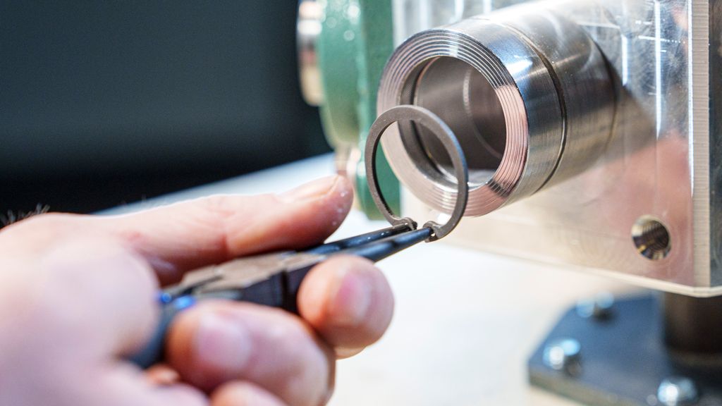 Ei hånd holder ei tang som holder en ring. Foto.