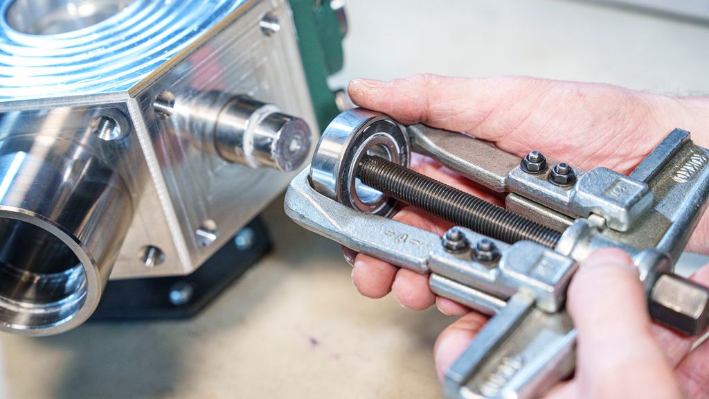 Ei hånd som holder et verktøy med to bein festa til et lager. Foto.